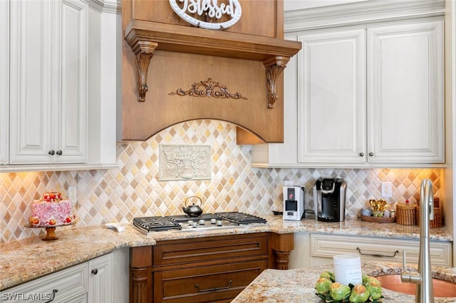 kitchen with light stone countertops, backsplash, white cabinetry, and stainless steel gas cooktop