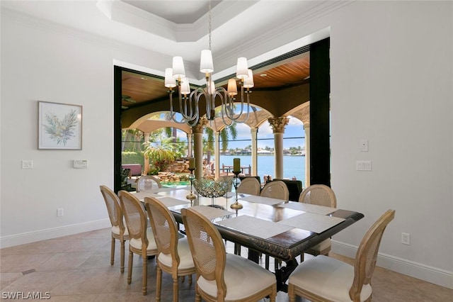 tiled dining space with a water view, a raised ceiling, a chandelier, and ornamental molding