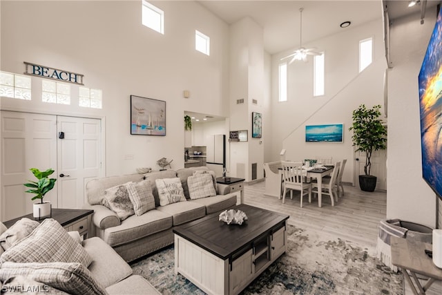 living room with light hardwood / wood-style flooring, ceiling fan, and a towering ceiling