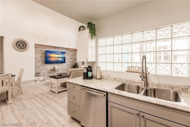 kitchen with sink, light hardwood / wood-style flooring, stainless steel dishwasher, and light stone countertops