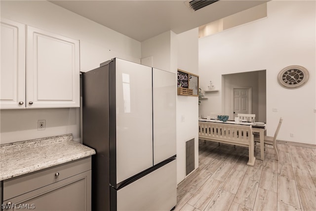 kitchen featuring white refrigerator, light stone counters, light hardwood / wood-style flooring, and white cabinetry