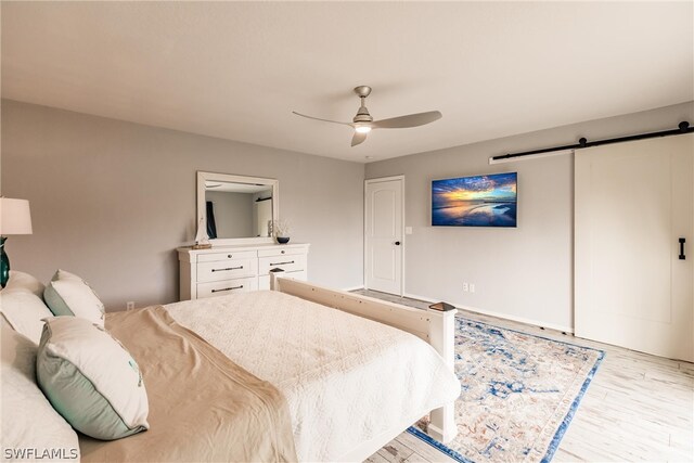 bedroom with light hardwood / wood-style flooring, ceiling fan, and a barn door