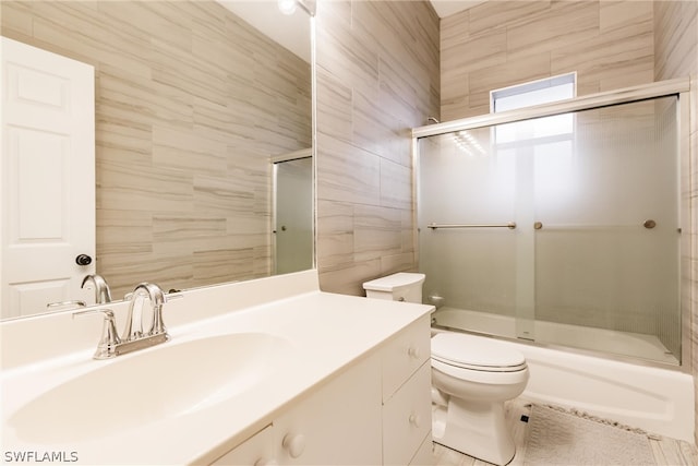 full bathroom featuring tile floors, tile walls, vanity, bath / shower combo with glass door, and toilet