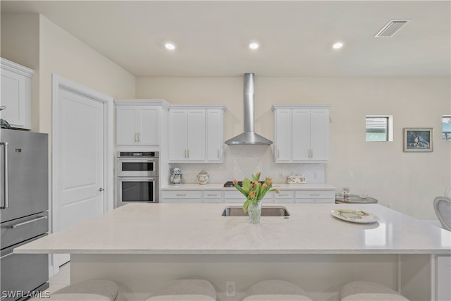 kitchen featuring appliances with stainless steel finishes, wall chimney range hood, a breakfast bar area, and an island with sink