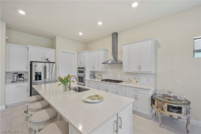 kitchen featuring tasteful backsplash, stainless steel appliances, wall chimney range hood, and white cabinetry