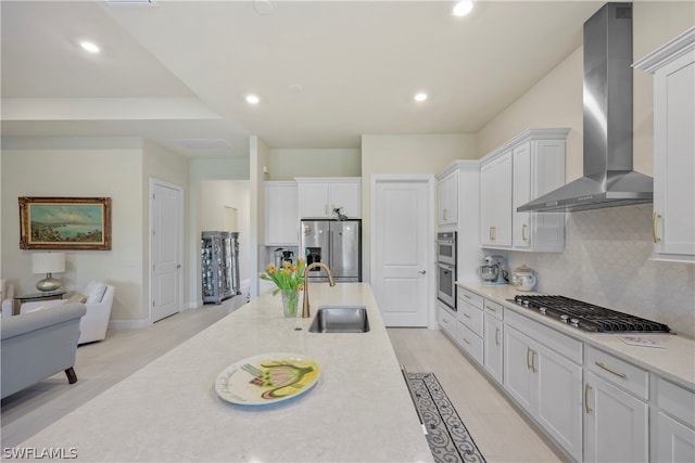 kitchen with white cabinets, sink, stainless steel appliances, and wall chimney range hood