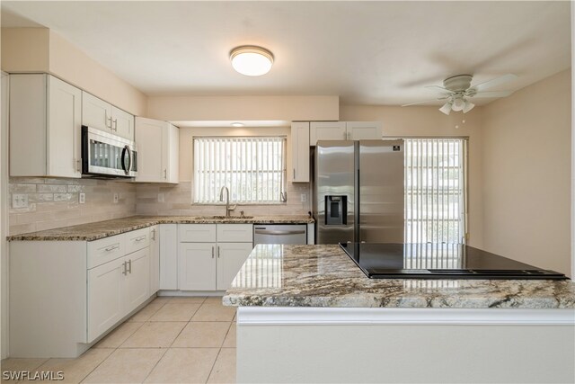 kitchen with appliances with stainless steel finishes, tasteful backsplash, light tile flooring, and white cabinets