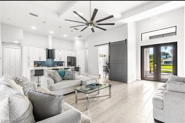 living room with french doors, a barn door, ceiling fan, beamed ceiling, and light wood-type flooring