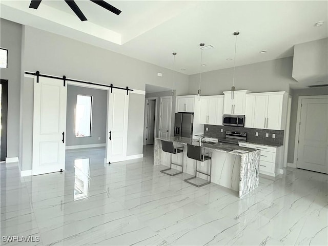 kitchen with an island with sink, stainless steel appliances, white cabinets, dark stone counters, and a barn door