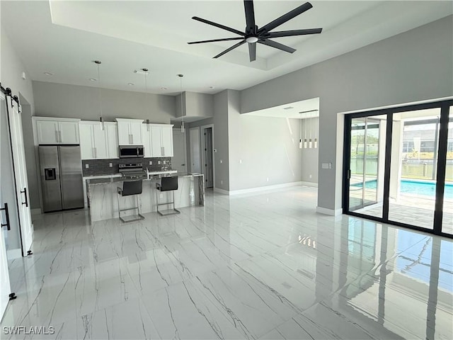 kitchen with stainless steel appliances, white cabinets, a barn door, a kitchen island, and a kitchen bar