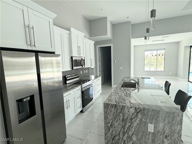 kitchen featuring appliances with stainless steel finishes, sink, white cabinetry, hanging light fixtures, and a kitchen island with sink