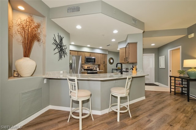 kitchen with kitchen peninsula, a breakfast bar area, stainless steel appliances, wood-type flooring, and sink