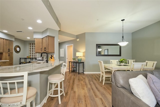 kitchen with light stone counters, light hardwood / wood-style floors, pendant lighting, and a breakfast bar area