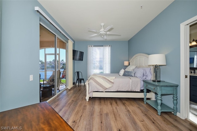 bedroom with hardwood / wood-style floors, ceiling fan, a water view, and access to exterior