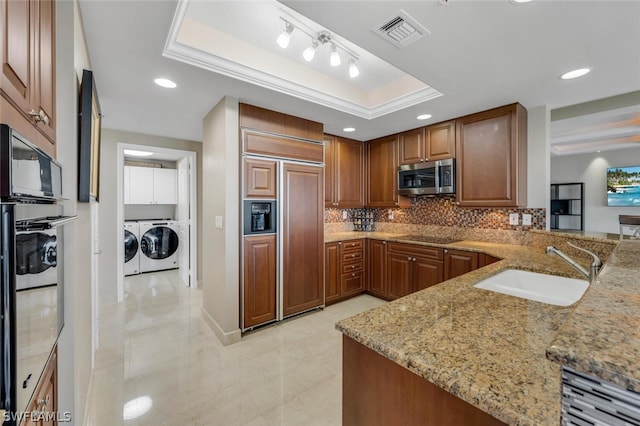 kitchen with a raised ceiling, sink, independent washer and dryer, kitchen peninsula, and stainless steel appliances