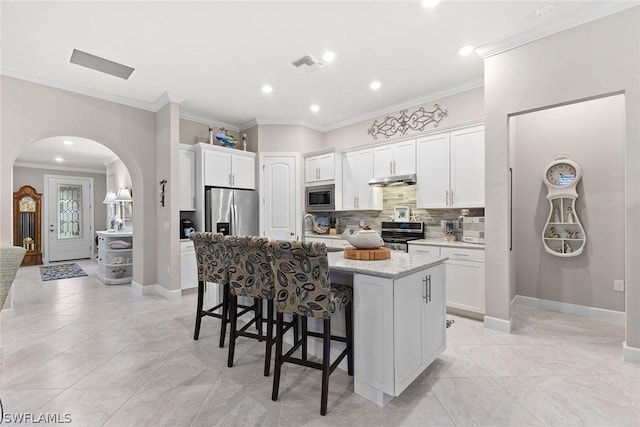 kitchen with light stone counters, stainless steel appliances, white cabinets, a kitchen island with sink, and decorative backsplash