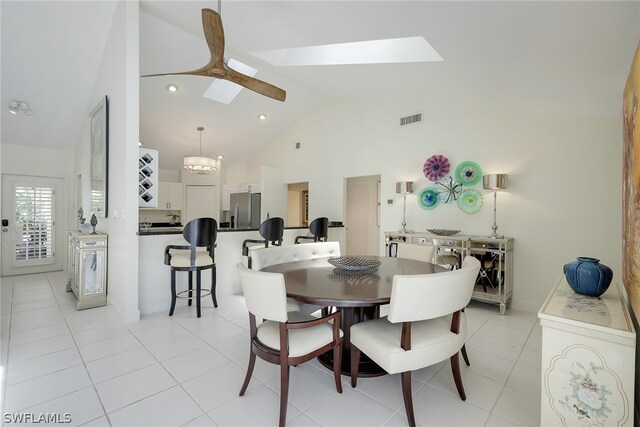 tiled dining space with a skylight, high vaulted ceiling, and ceiling fan with notable chandelier