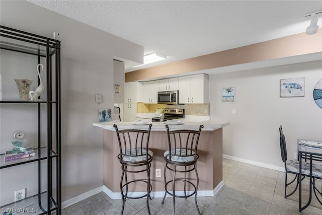 kitchen with appliances with stainless steel finishes, white cabinets, backsplash, and light tile floors