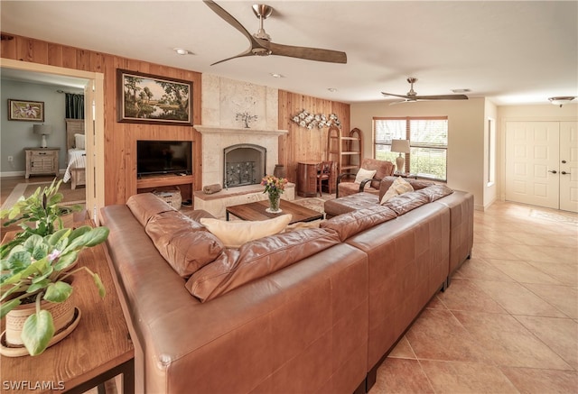 tiled living room with ceiling fan, a fireplace, and wood walls