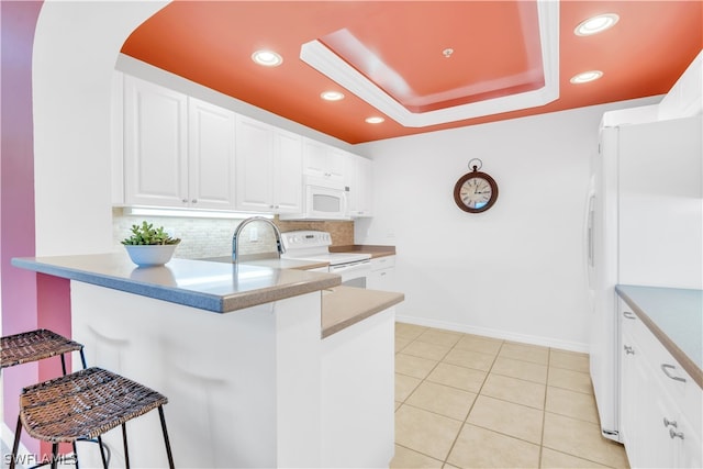 kitchen with backsplash, white appliances, light tile flooring, white cabinetry, and a raised ceiling