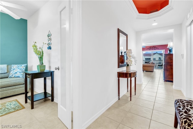 corridor with crown molding, light tile floors, and a tray ceiling