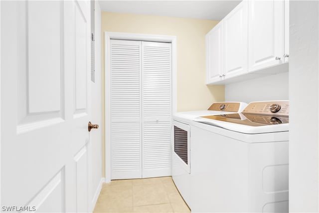 clothes washing area featuring cabinets, light tile floors, and washer and clothes dryer