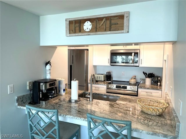 kitchen with white cabinetry, stainless steel appliances, a kitchen breakfast bar, sink, and stone counters