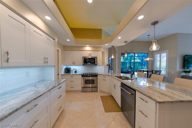 kitchen with stainless steel appliances, white cabinetry, sink, and decorative light fixtures