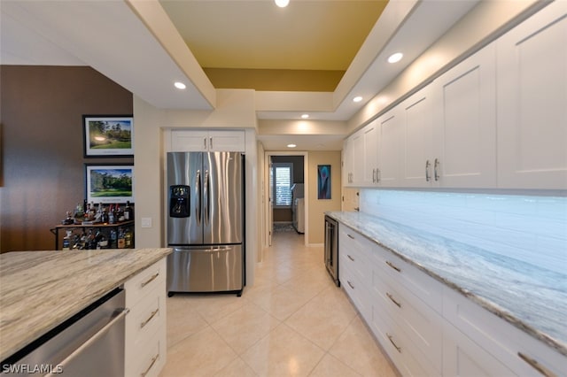 kitchen with light tile patterned flooring, appliances with stainless steel finishes, light stone countertops, and white cabinets