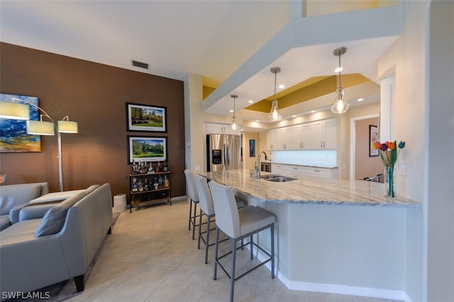 kitchen featuring a breakfast bar, sink, decorative light fixtures, stainless steel fridge with ice dispenser, and white cabinets