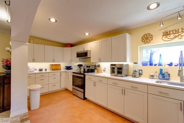 kitchen with appliances with stainless steel finishes, light tile floors, sink, white cabinetry, and decorative columns