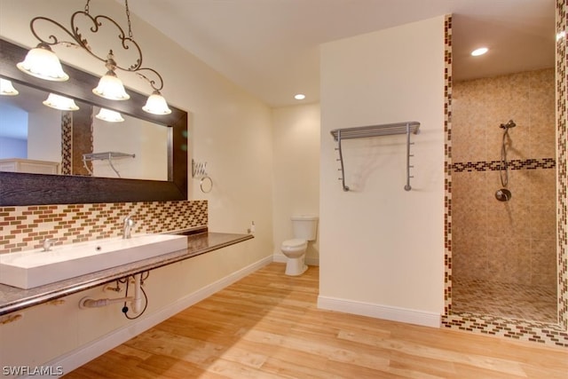 bathroom featuring wood-type flooring, backsplash, toilet, and a tile shower