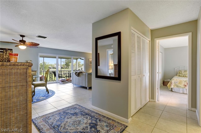 corridor featuring light tile patterned floors, visible vents, baseboards, and a textured ceiling