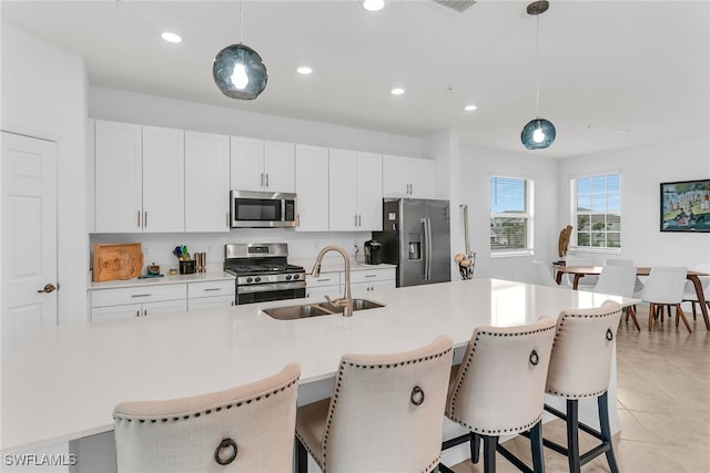 kitchen featuring appliances with stainless steel finishes, a sink, a kitchen breakfast bar, white cabinetry, and decorative light fixtures