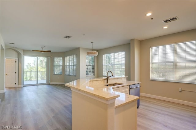 kitchen featuring light stone counters, sink, light hardwood / wood-style floors, dishwasher, and hanging light fixtures