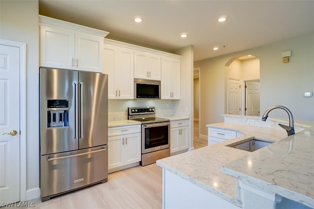 kitchen featuring appliances with stainless steel finishes, white cabinets, sink, light hardwood / wood-style flooring, and light stone countertops