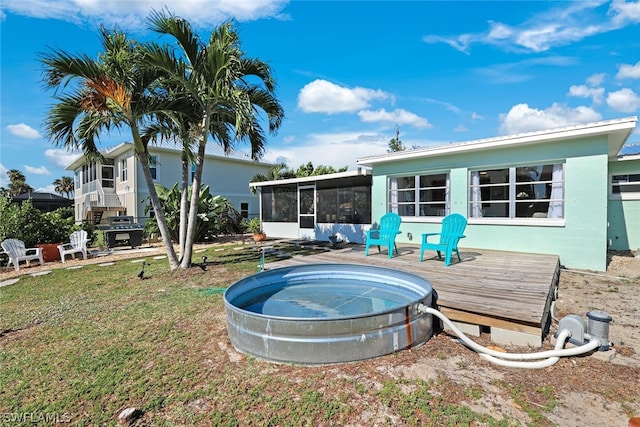 back of house featuring a hot tub, a deck, a lawn, and a sunroom