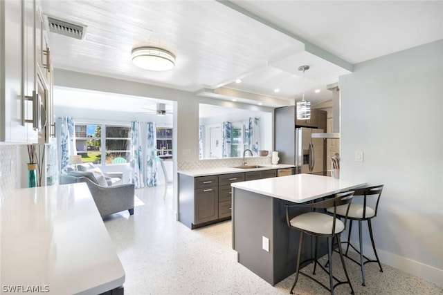 kitchen featuring decorative backsplash, a kitchen breakfast bar, dark brown cabinets, stainless steel fridge, and sink