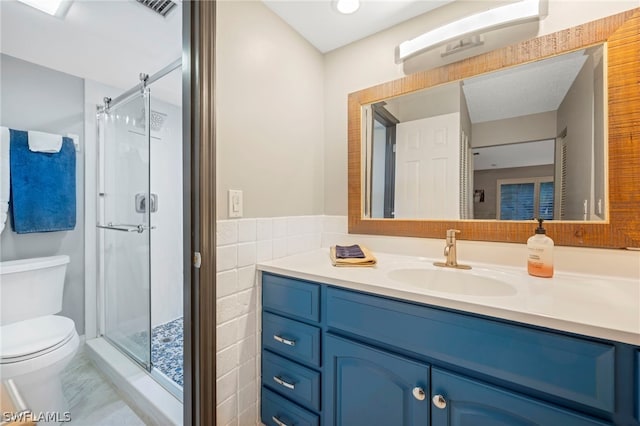 bathroom with tile floors, tile walls, vanity, a shower with shower door, and toilet