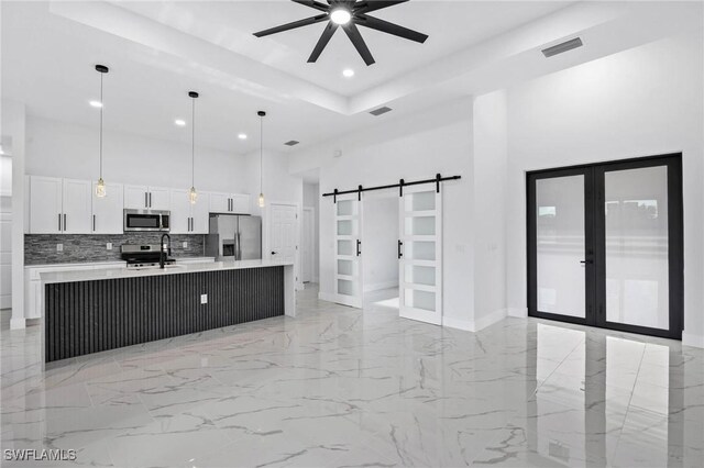 kitchen with white cabinets, a barn door, stainless steel appliances, ceiling fan, and a kitchen island with sink