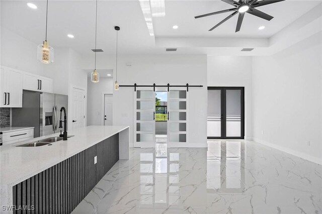 kitchen featuring stainless steel fridge with ice dispenser, a barn door, ceiling fan, light stone counters, and white cabinets