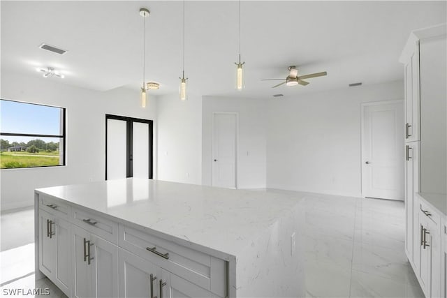 kitchen with pendant lighting, a center island, white cabinets, ceiling fan, and light stone counters