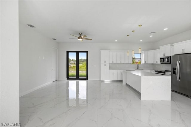 kitchen with white cabinetry, hanging light fixtures, plenty of natural light, a kitchen island, and appliances with stainless steel finishes