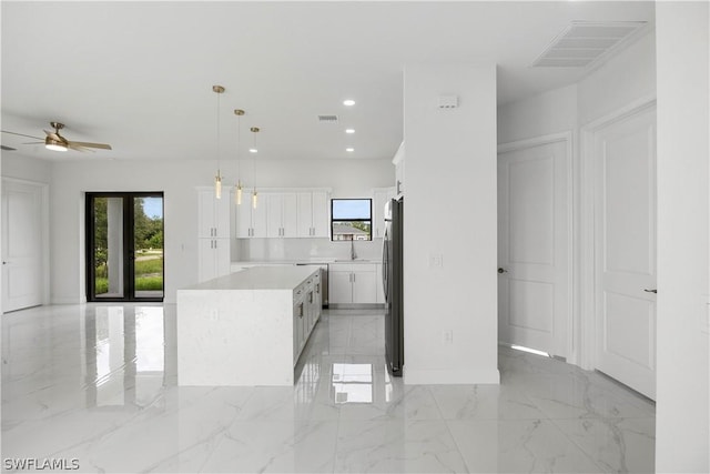 kitchen featuring white cabinets, ceiling fan, stainless steel fridge, decorative light fixtures, and a kitchen island