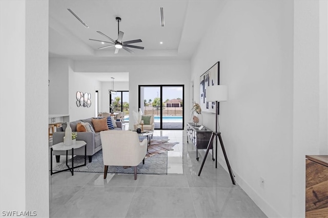 living room featuring ceiling fan, a tray ceiling, and light tile floors