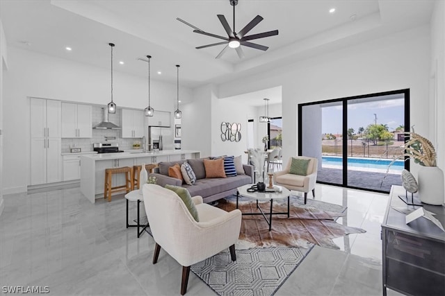 living room with a towering ceiling, ceiling fan, a tray ceiling, sink, and light tile floors