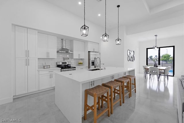 kitchen with wall chimney exhaust hood, stainless steel appliances, a kitchen island with sink, and hanging light fixtures