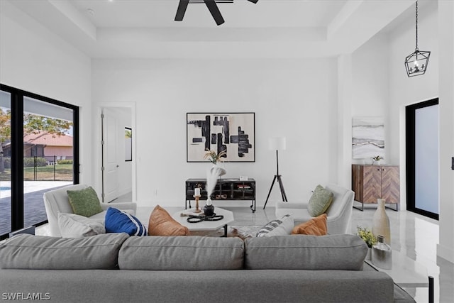 living room with a towering ceiling, tile flooring, ceiling fan, and a raised ceiling