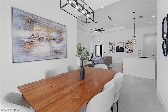 dining space with sink, ceiling fan with notable chandelier, light tile floors, and a raised ceiling