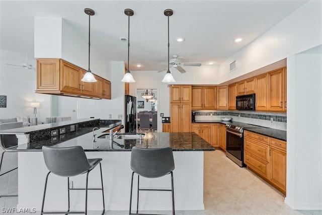 kitchen with a kitchen breakfast bar, ceiling fan, black appliances, dark stone countertops, and hanging light fixtures